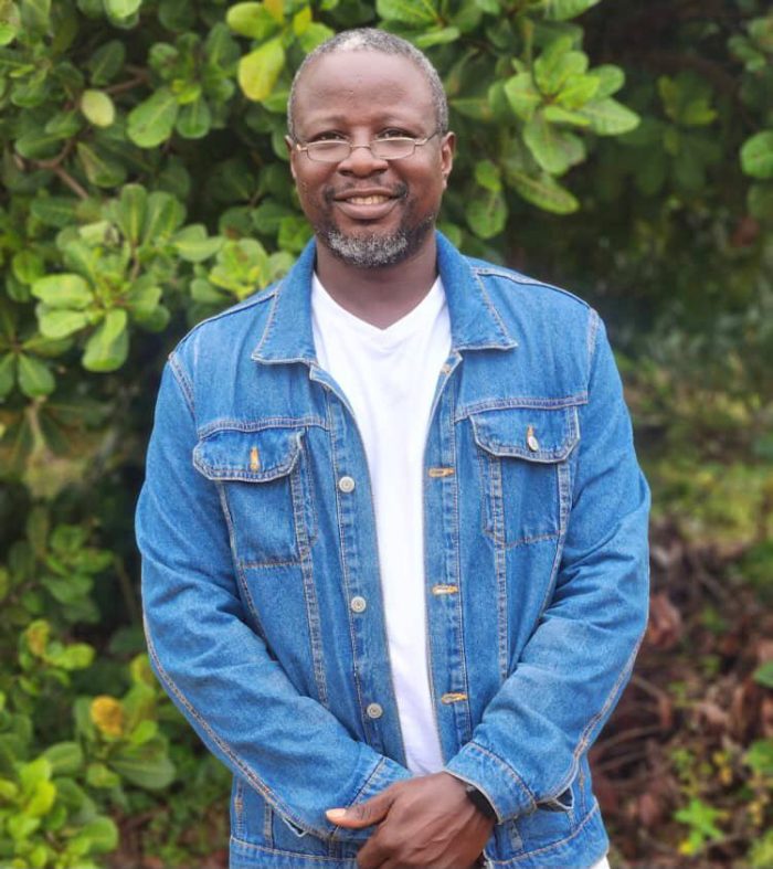 Olabode Ojoniyi stands in a jean jacket in front of greenery